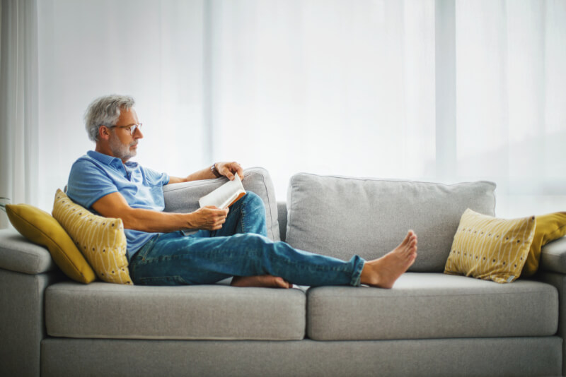 Mature man reading a book on the sofa.